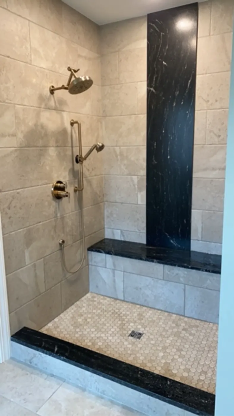 Finished walk-in shower with a black stone accent wall and bench