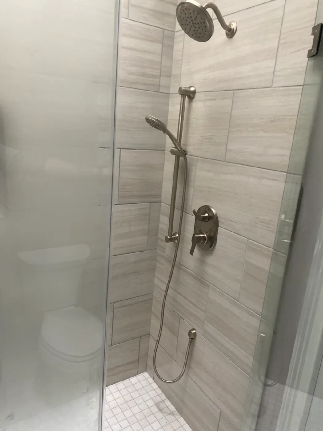 Glass-enclosed tiled shower with a handheld shower