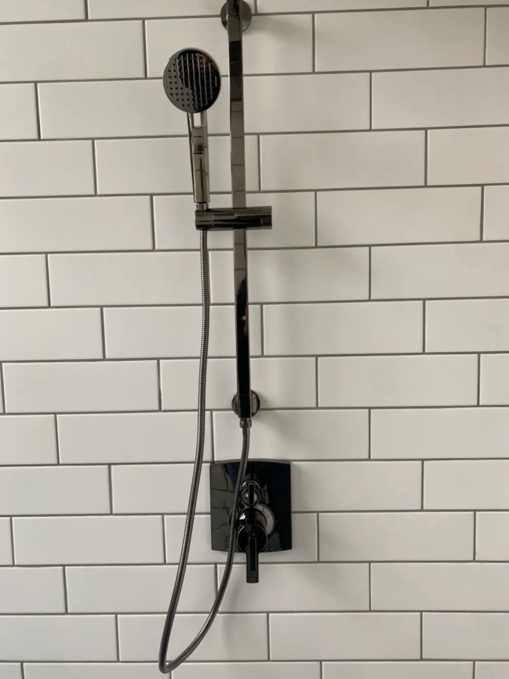 White tile shower with a black rain head and valve